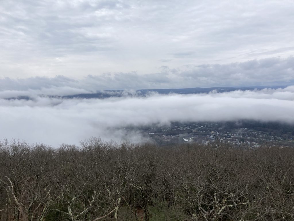 Looking down into a low valley among rolling hills.  A village can be seen through gaps in a low hanging cloud.