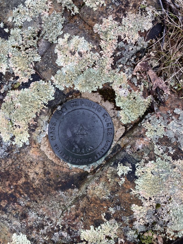 A brass surveying monument set into bedrock at the top of the mountain from the Massachusetts Department of Public Works