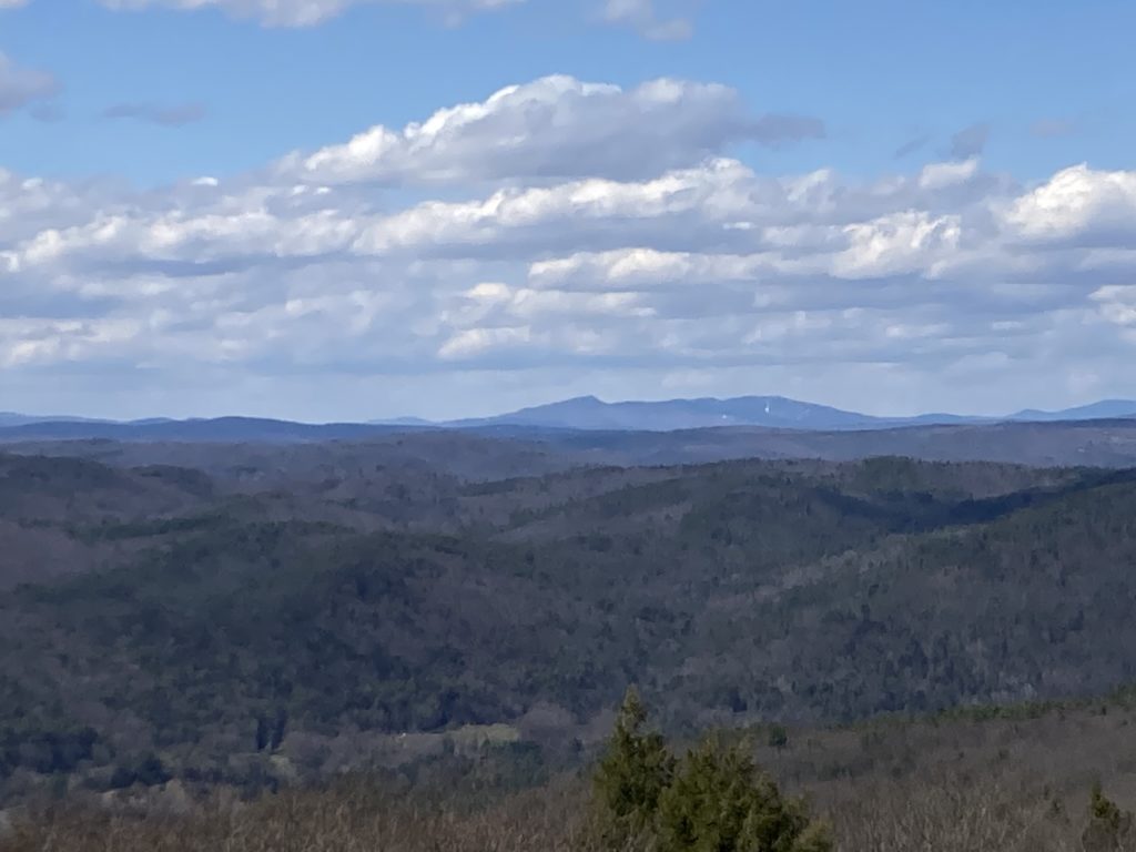 A snaggletooth mountain rises in the distance over rugged New England hills