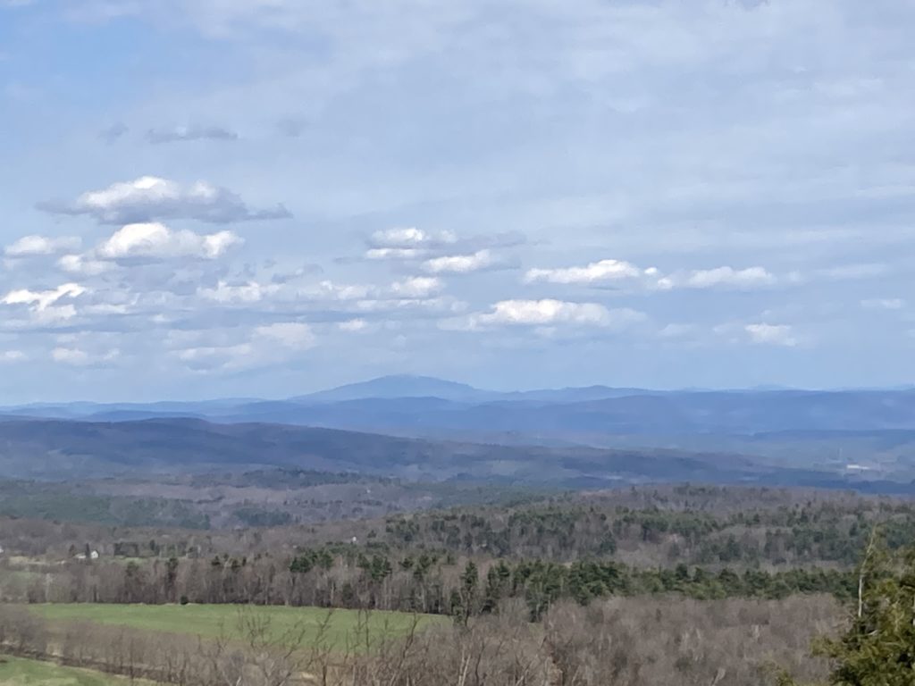 A conical shaped mountain looms large out of the distant haze over a subdued New England Landscape