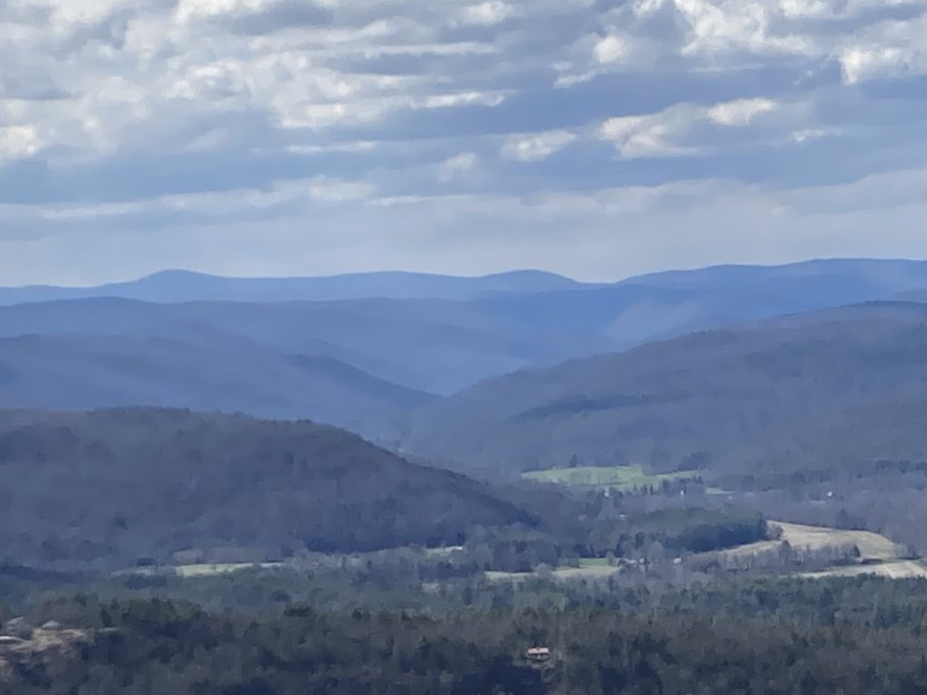 A river valley winds its way among mountains stretching off into the distance under a cloudy sky