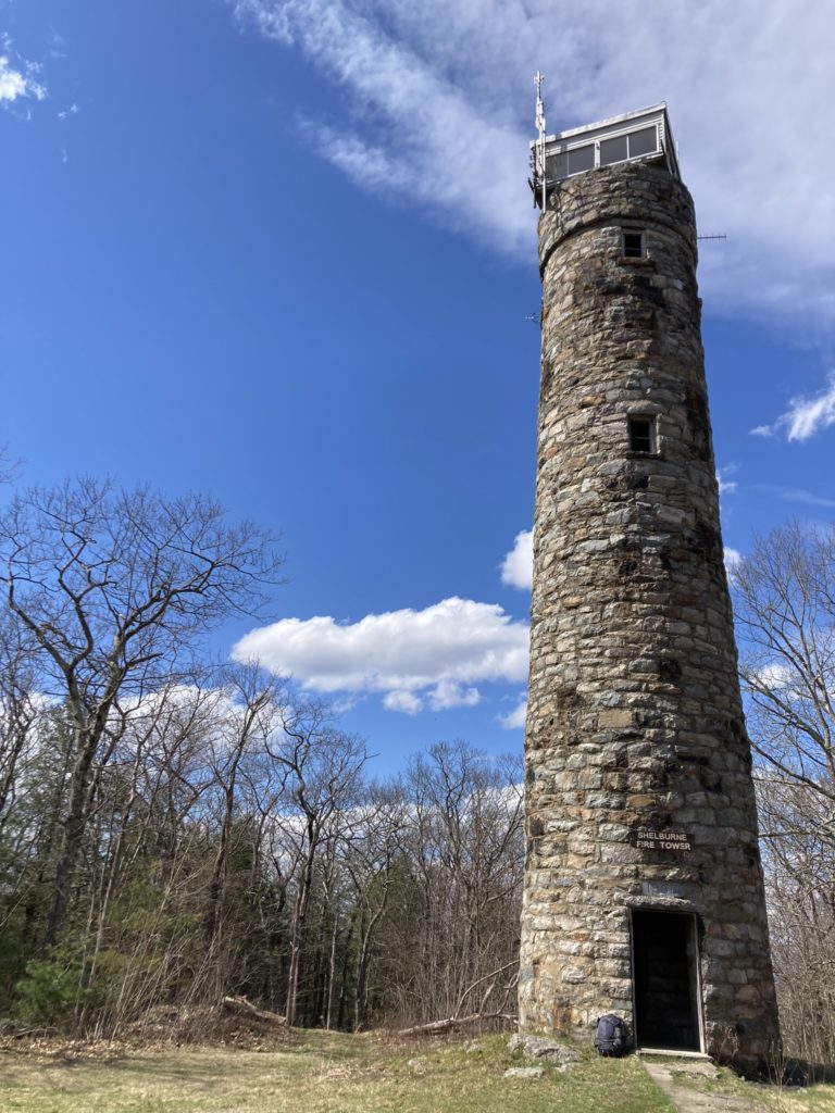 The stone tower, illuminated by the sun with a blue sky, with white clouds, in the background